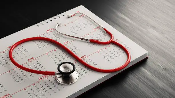 Red stethoscope and a calendar on black wood surface. Horizontal composition with copy space. Health and reminder concept with selective focus.