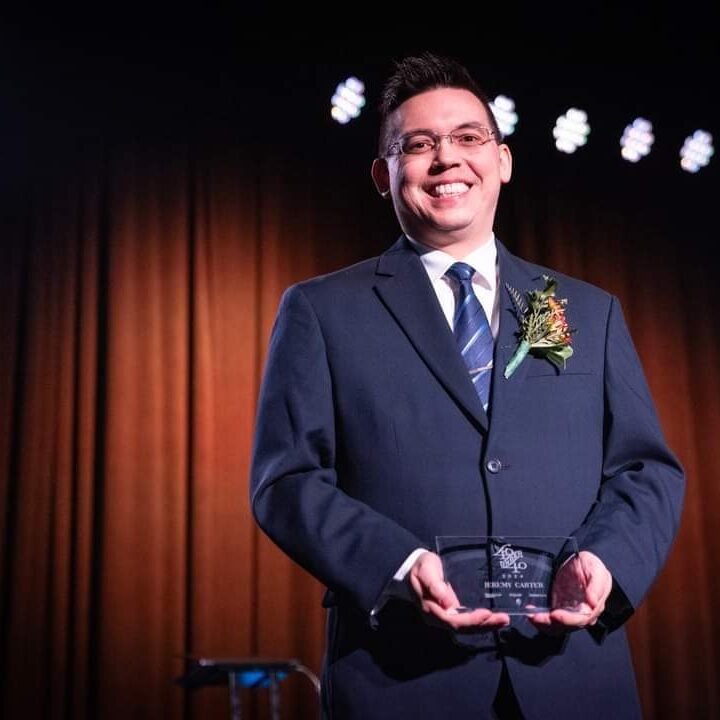 Smiling man in suit holding award on stage