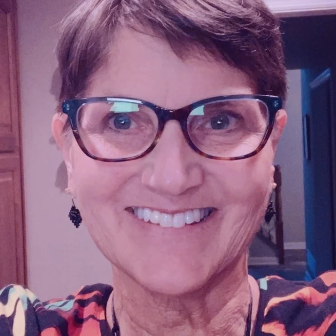 Smiling short-haired person wearing glasses and earrings